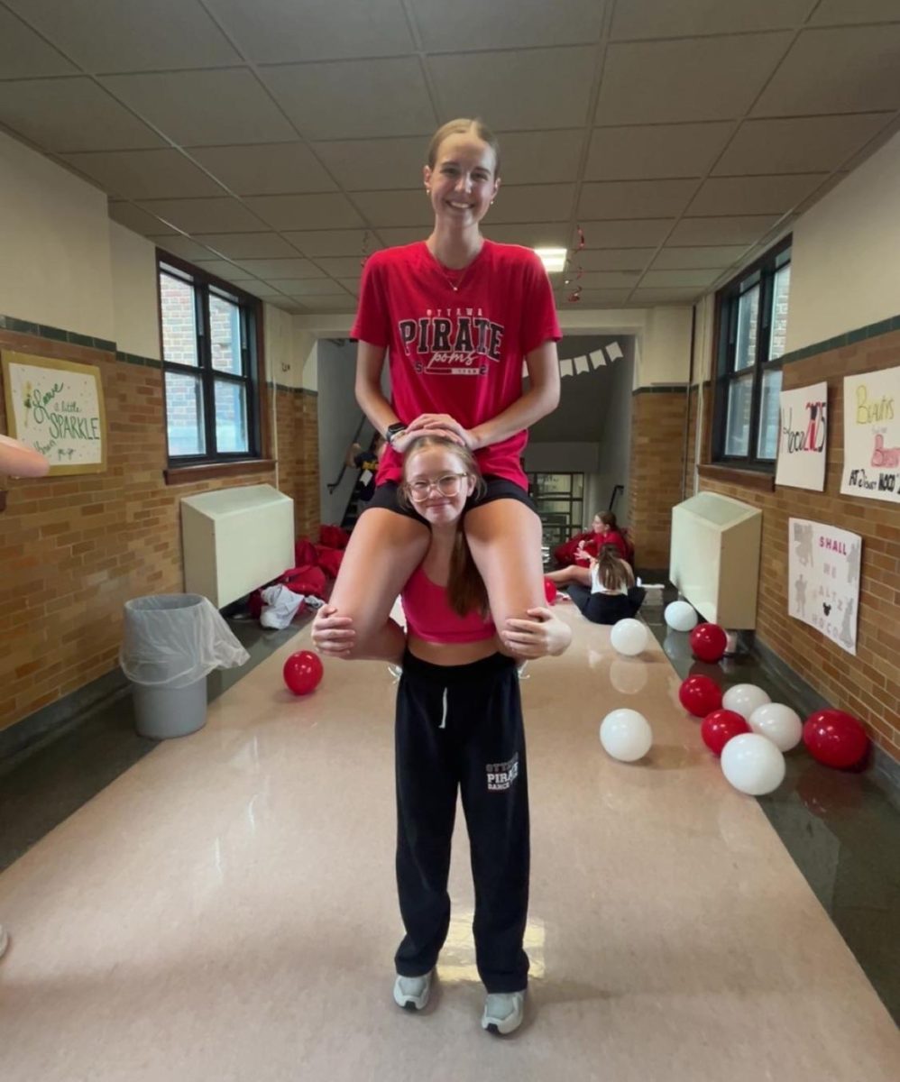  What is she doing up there? Sophomore Makenzee Rausch and Senior Madilyn Theissen pose for the camera while decking out the halls for homecoming. Poms were asked to help and make posters for the hallways. Rausch said, “My favorite part of setting up was learning the 'Teen Beach' dance for our video.” Said Rausch  