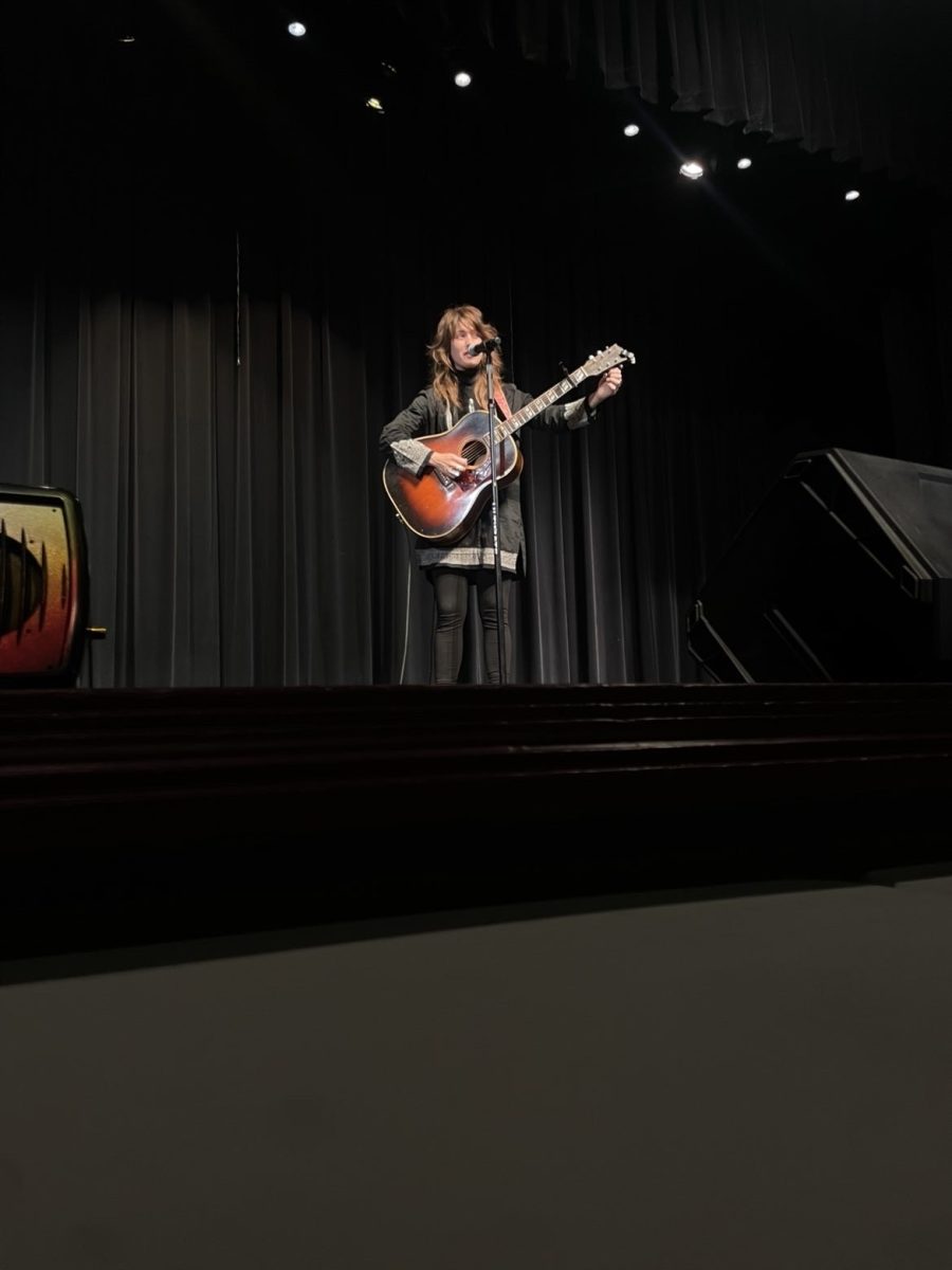Christina Eltrevoog singing and playing guitar while performing her original songs on the first day of Fine Arts. 