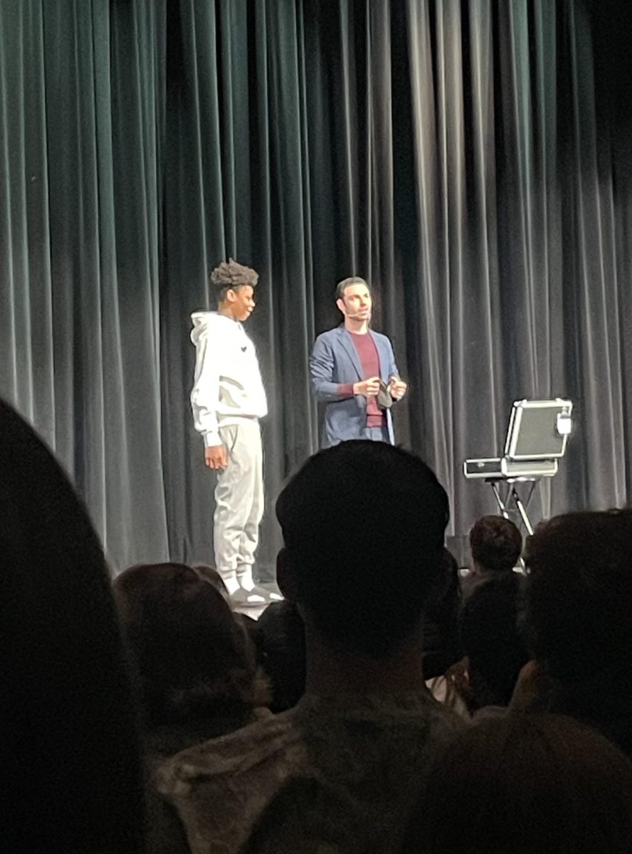 Freshman Timarrius Hinton stands on stage with magician David Anthony as Anthony sets up a magic trick. 
